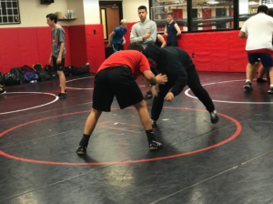 Wrestlers practicing takedowns as one of their beginning drills for the day. Observers looking out for tips on how to improve their movements.
