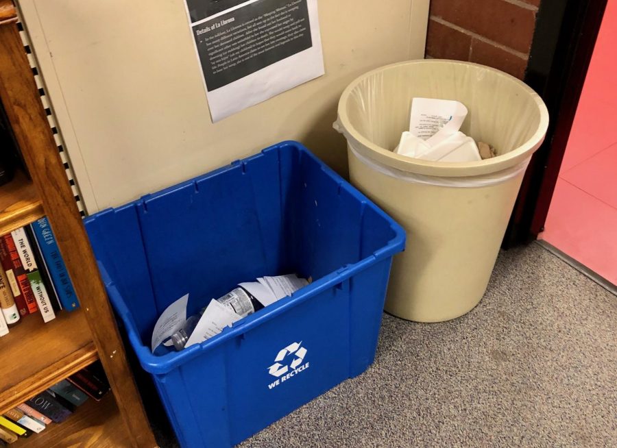 Feature Photo by Brianna Sanchez - A recycling bin and a trash can are placed side by side in an English classroom. The recycling bin contains paper and a water bottle, while the trash can also hold paper.