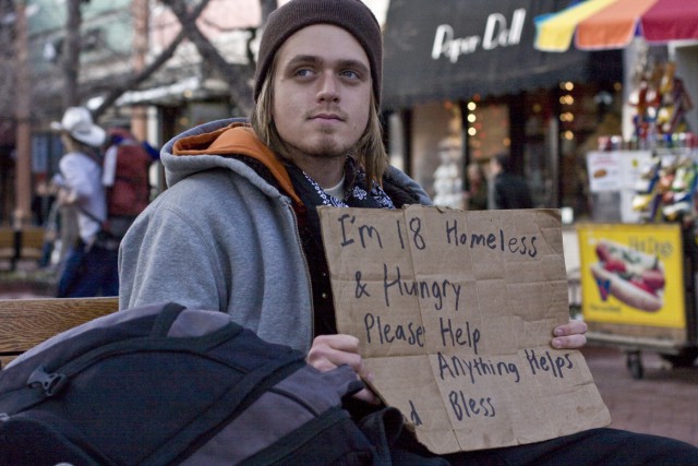 An 18 year old man stands outside some businesses downtown with a cardboard sign in hopes of receiving some donations. Feature Story: (Boulder Weekly)