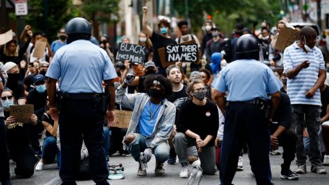 Black Lives Matter protesters are on their knees holding signs. The fist, a symbol of black power and resistance to injustice is held up by many of the protesters. (ABC News)