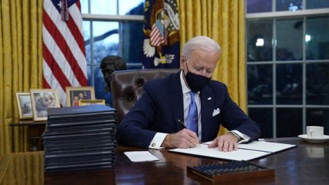 President Joe Biden sits in the Oval Office while signing several documents. (AP News)